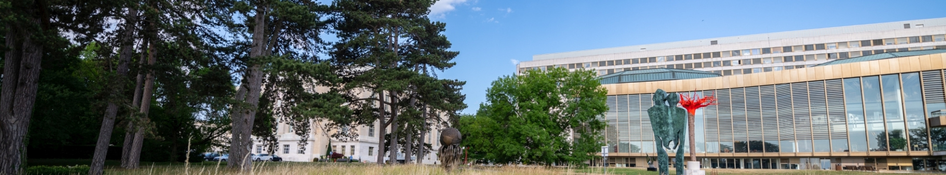 A panoramic view of one of the buildings inside the Palais des Nations next to some trees and behind some artwork.